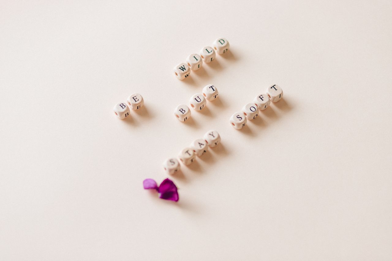 Le temps d'une rencontre Wooden letter dice spell out Be Wild But Stay Soft on a calm background with petals.